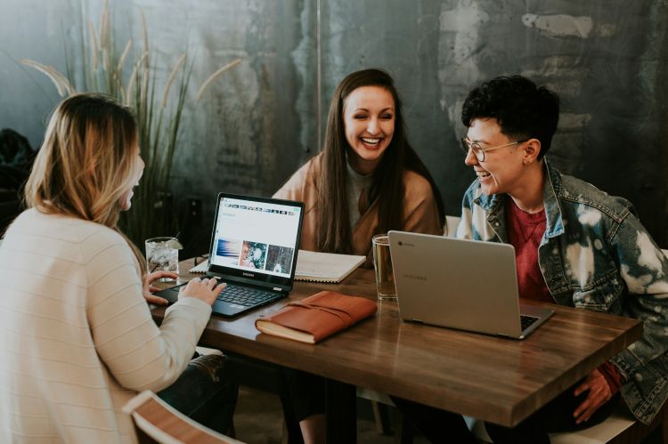 Three employees with laptops working at a table and laughing