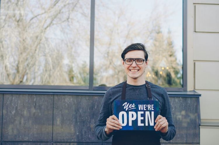 a smiling man holding a sign that says Yes, We're Open