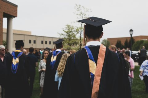 college graduates standing outdoors surrounded by friends and family