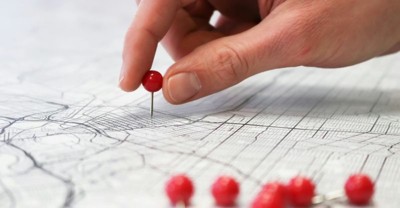 a person's hand placing a push-pin into a city street map