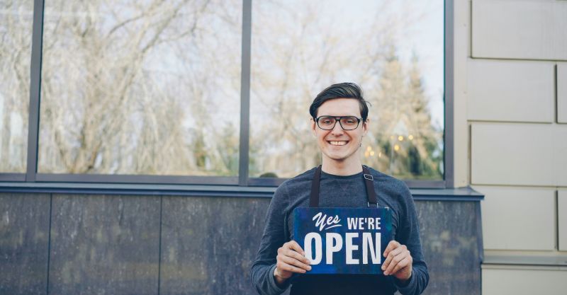 a smiling man holding a sign that says Yes, We're Open