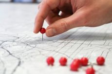 a person's hand placing a push-pin into a city street map