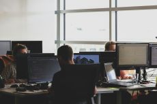 Employees in an open office space sitting on chairs in front of computer monitors.