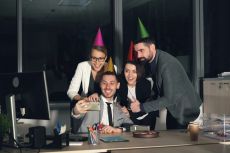 a group of coworkers wearing party hats taking a selfie